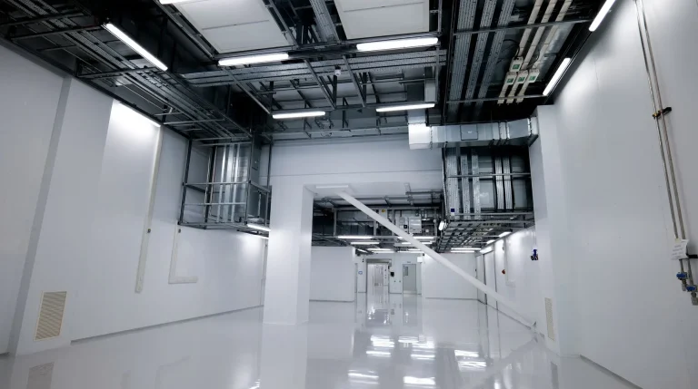 Inside one of the clean and dry zones at the UK Battery Industrialisation Centre (UKBIC), with white walls and floor and cabling and pipework across the ceiling.