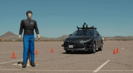 A car approaches a standing test dummy in a desert location