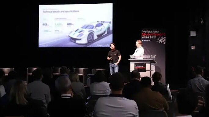 Two men stand on a stage at PMW Expo delivering a lecture.