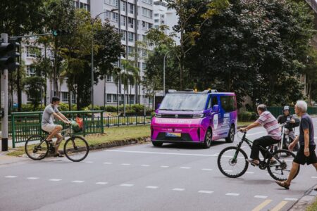 An Ai.R AV – a WeRide GXR – on a test run in Punggol, Singapore. The vehicle is at an intersection with bicycles and pedestrians crossing the road in front of it