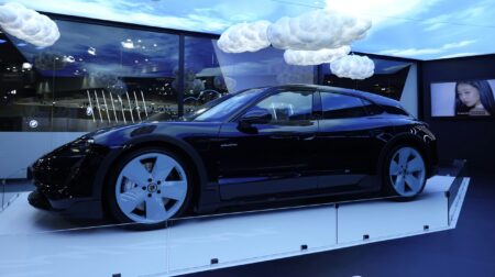 A dark electric vehicle sits on a display stand at a trade show, with clouds above demonstrating its connectivity