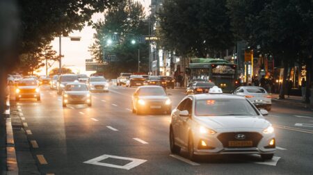 Cars on an urban street with their headlights on in a low-light environment.