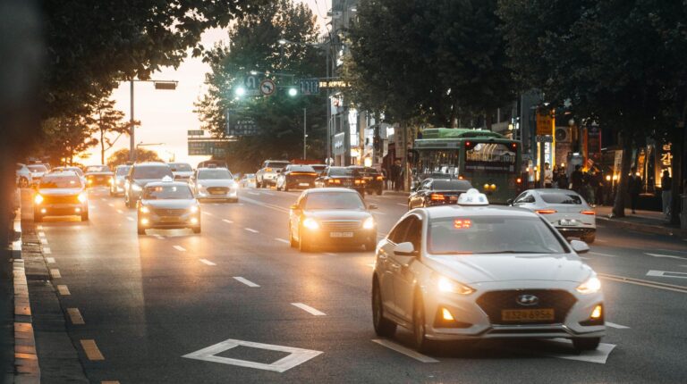 Cars on an urban street with their headlights on in a low-light environment.