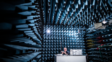 An engineer conducts electromagnetic compatibility testing inside an anechoic chamber, measuring device performance.