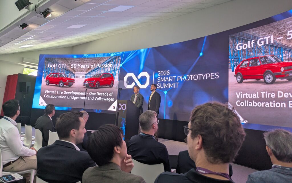 Two speakers stand on a stage at the VI-Grade Smart Prototypes Summit giving a presentation to a room of conference attendees.