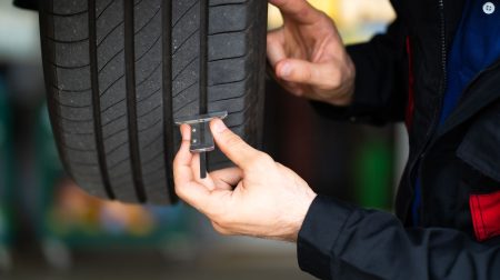 A man runs a piece of testing equipment along the side of a tire.