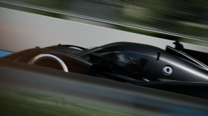 The black Peugeot 9X8 drives at speed on a test track. The background is blurred.
