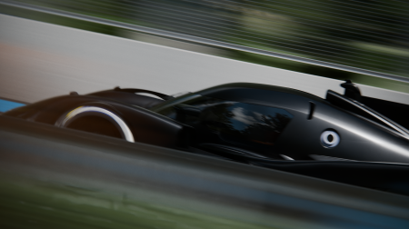 The black Peugeot 9X8 drives at speed on a test track. The background is blurred.